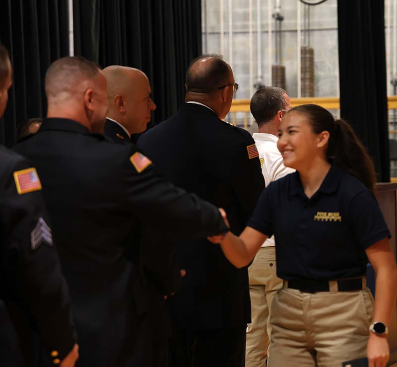 A young woman shakes hands with an adult on a stage.