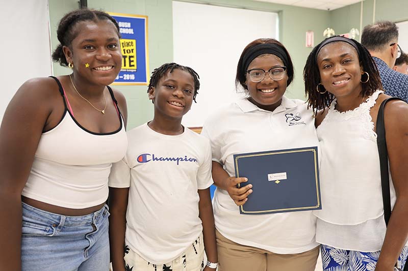 Four young women stand together smiling. One is holding a certificate.