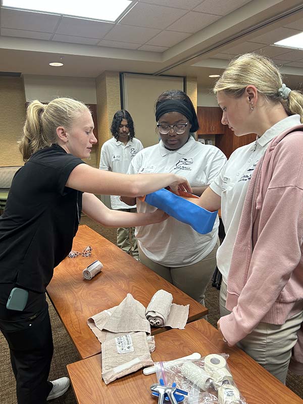 Two high school medical academy students put a cast on another student's arm.