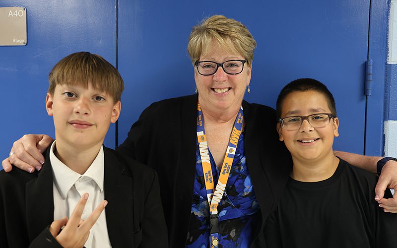 A woman wish short blonde hair and glasses stands with two fifth-grade boys. All are smiling.