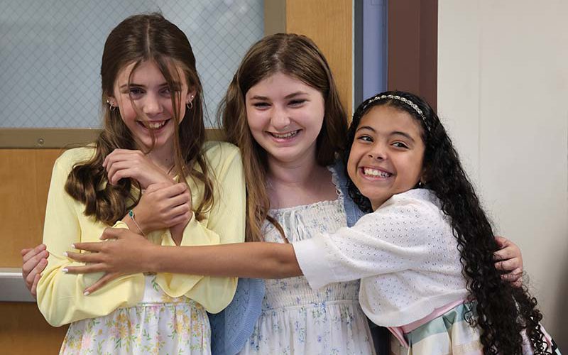 Three fifth-grade girls smile together and hug.