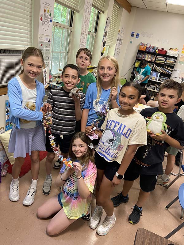 A group of fourth grade students hold up garlands of paper cranes they folded. They are smiling.