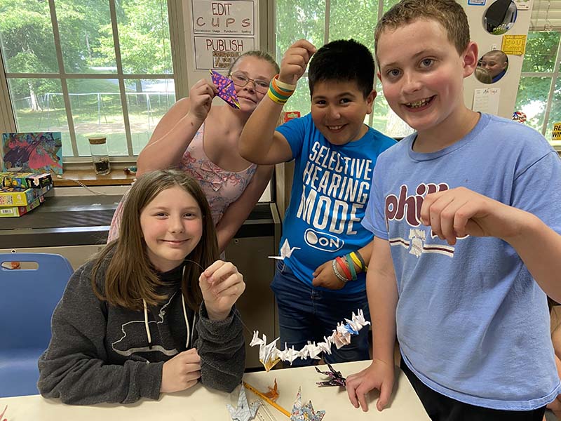 Fourth-grade students hold up strings that have paper cranes on them.