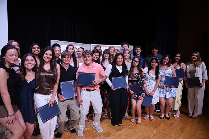 A group of 27 high school students standing on a stage. They are all holding certificates and smiling.