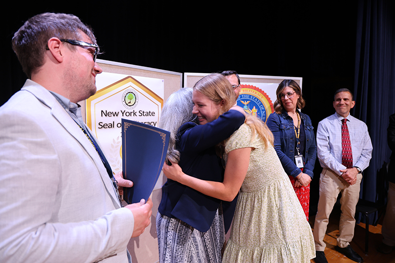 A woman hugs a high school student and others look on.