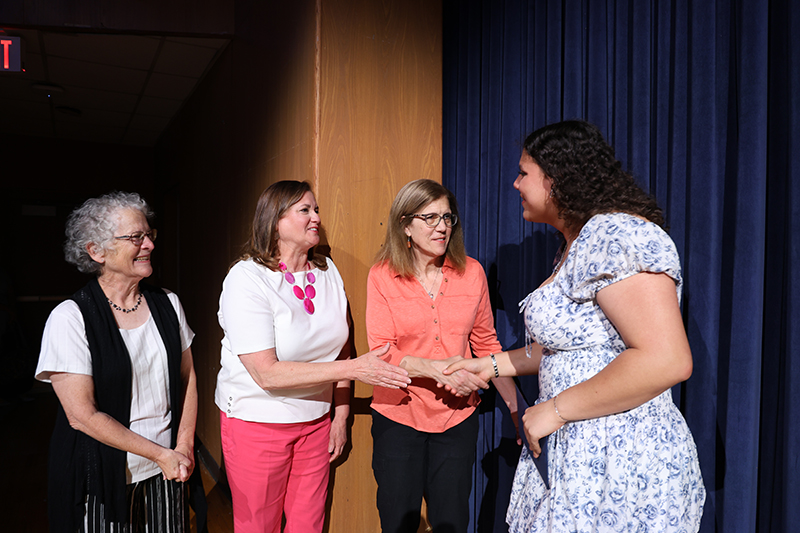 A young woman shakes hands with a woman, while two other women stand by and watch.