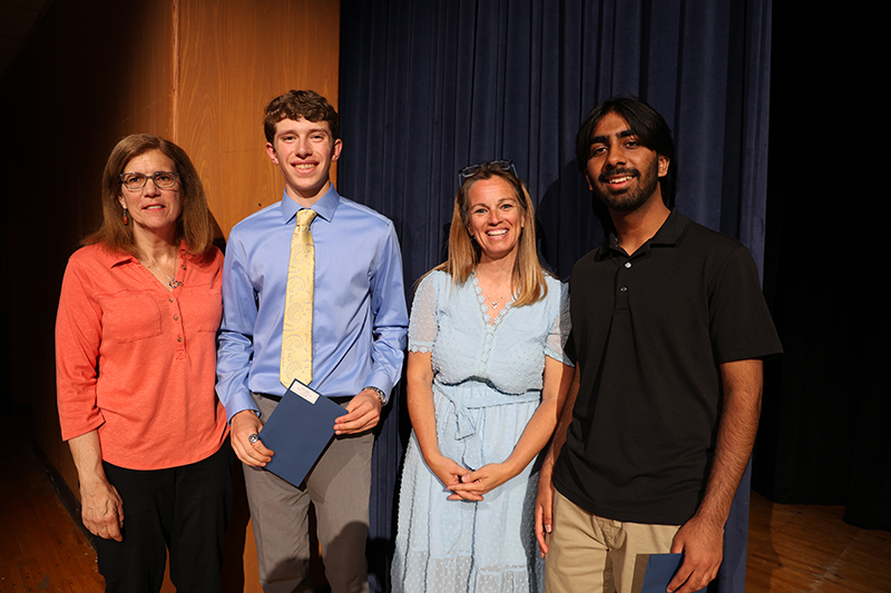 Two women stand with two high school senior boys on a stage. They are all smiling.