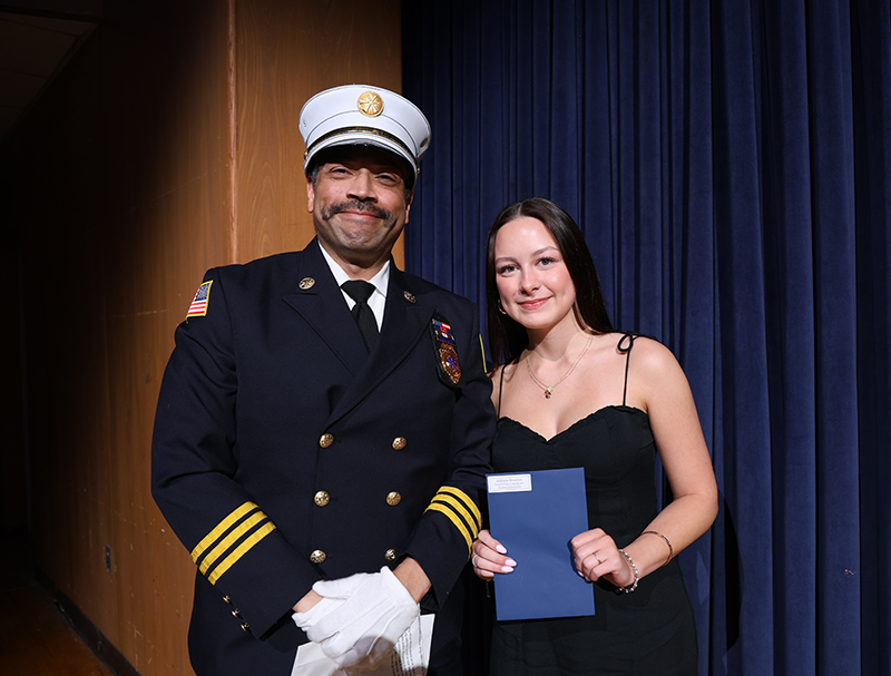 A man dressed in a firefighters uniform smiles and stands with a young woman who is holding a certificate.