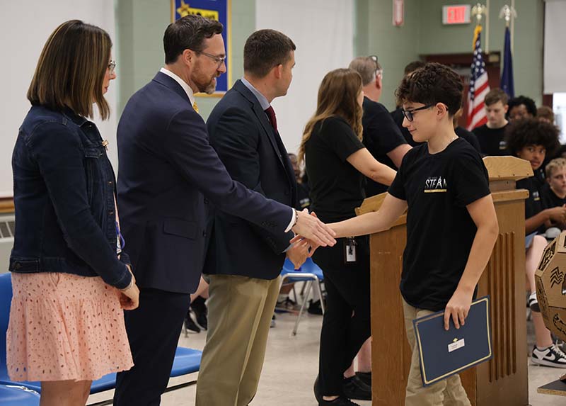 A man in a suit shakes hands with a young high school kid. There are others waiting to shake hands as well.