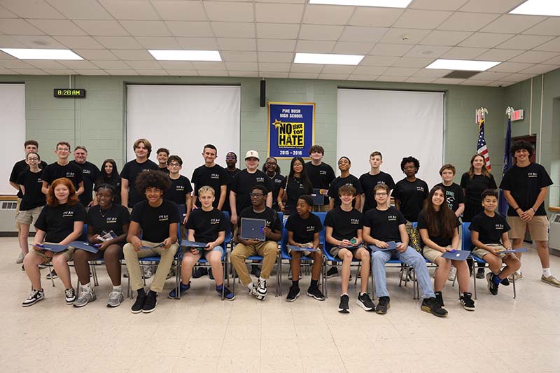 A group of 26 high school kids and two adults sit together smiling.