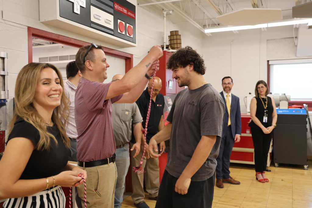 A high school senior smiles as a man puts a graduation cord over his head.