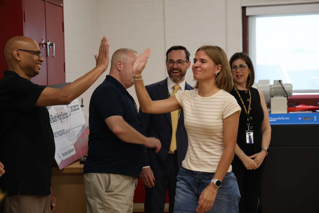 A high school senior girl high fives a man as others look on.