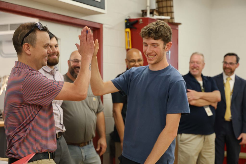 A high school senior boy smiles as he gives high fives to a man.