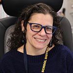 A woman with longer dark hair and glasses smiles.