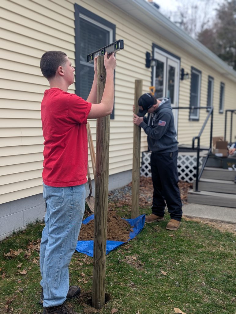 Two young men put large posts into the ground.