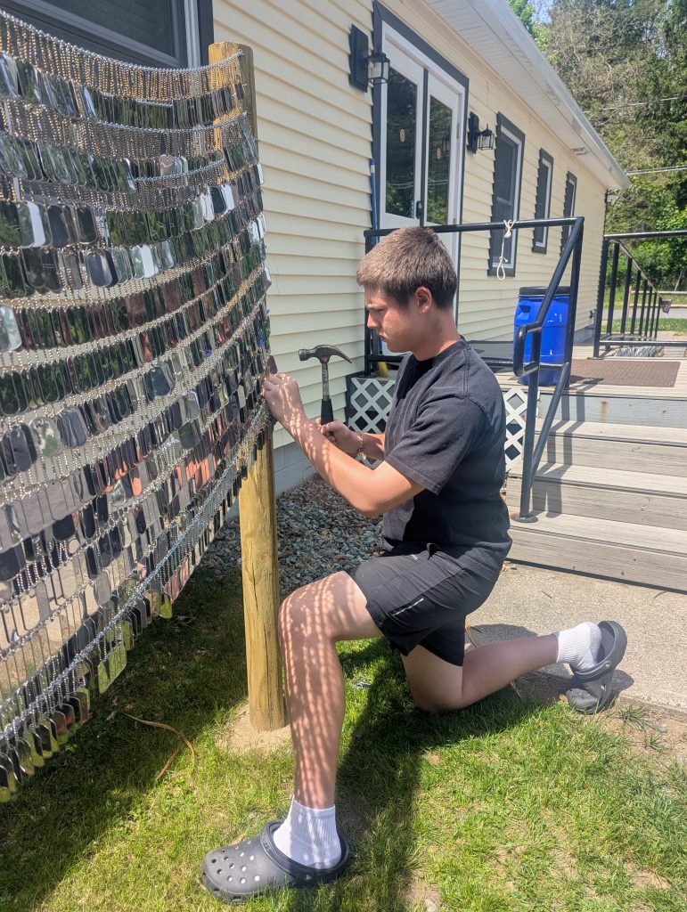 a young man attaches dog tags to chains that hang from posts.