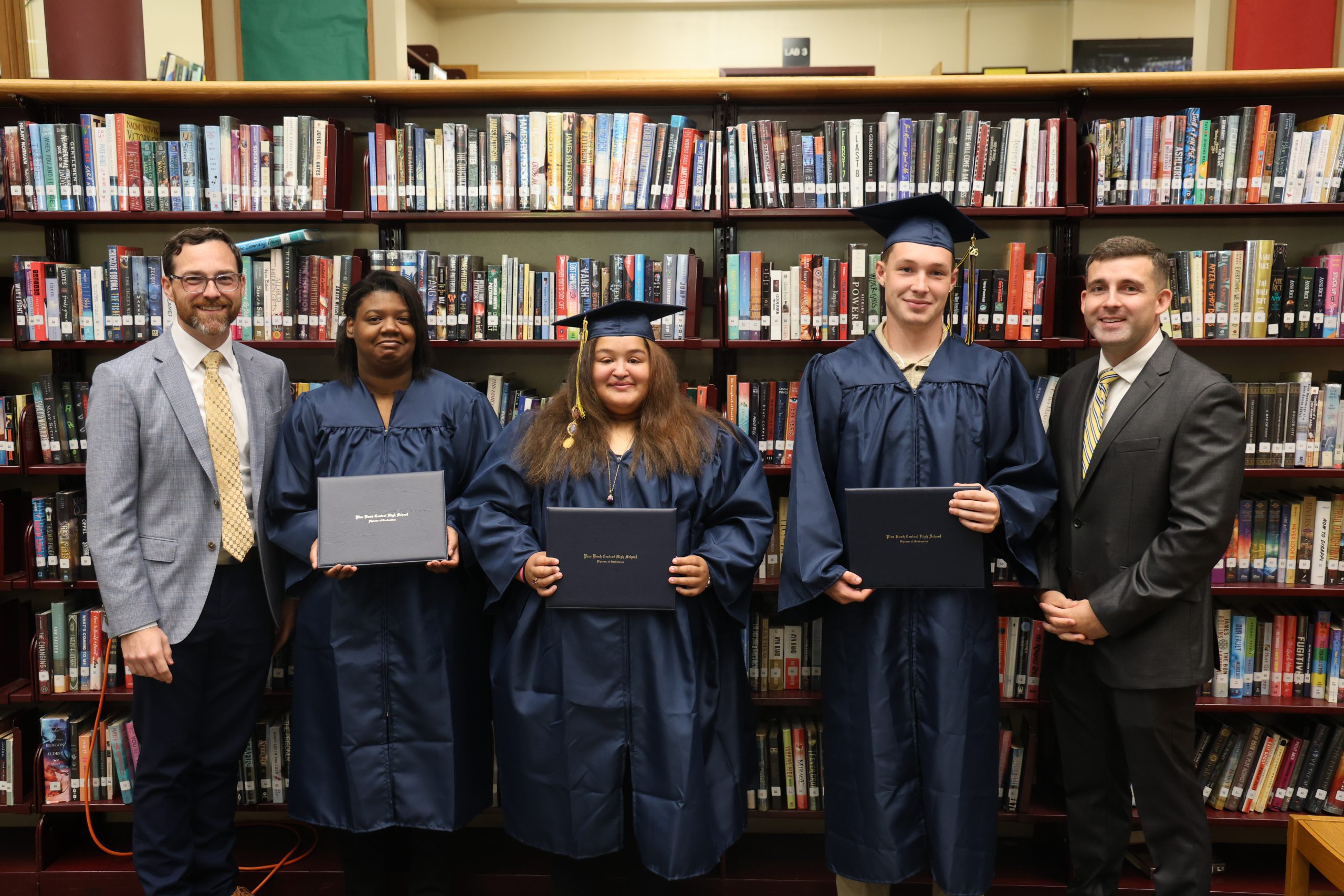 students in cap and gown posing for a picture with administrators