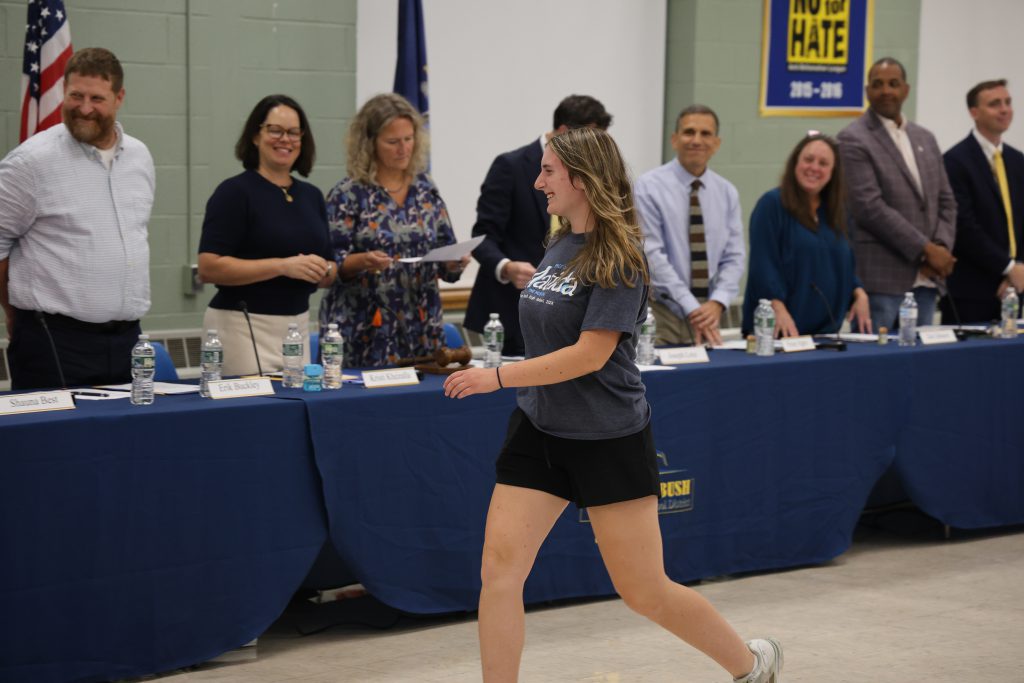 student walking toward a table with people standing