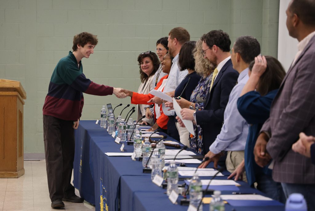 student giving hand shakes to a line of board members