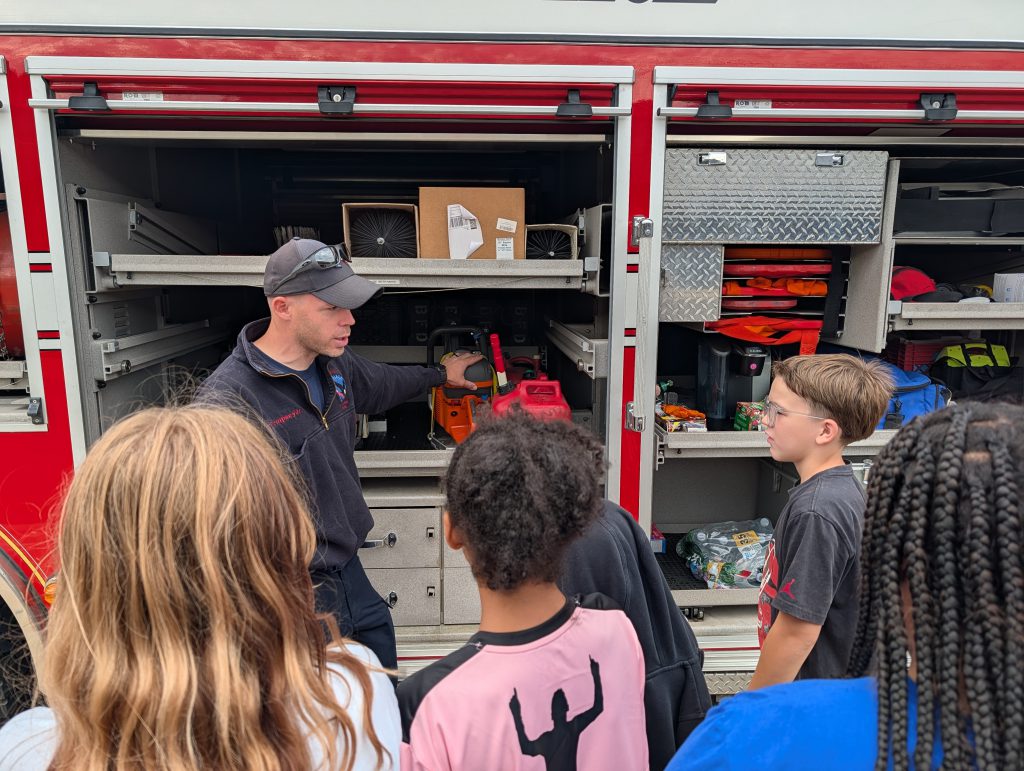 firefighter demonstrating equipment to elementary students