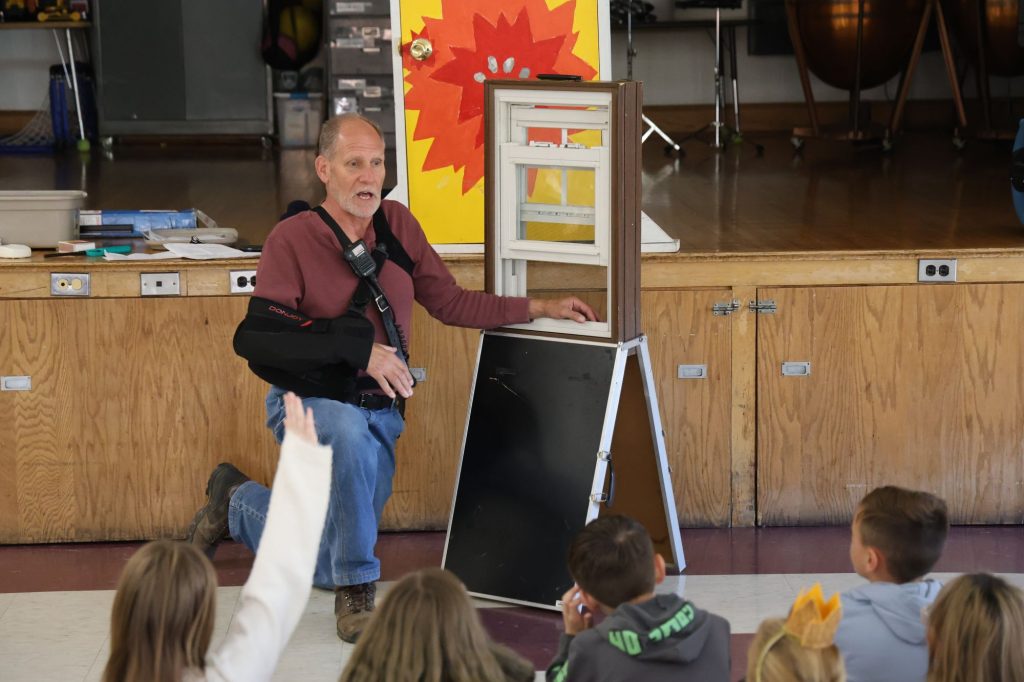 a firefighter demonstrates safety tips to elementary students using small window