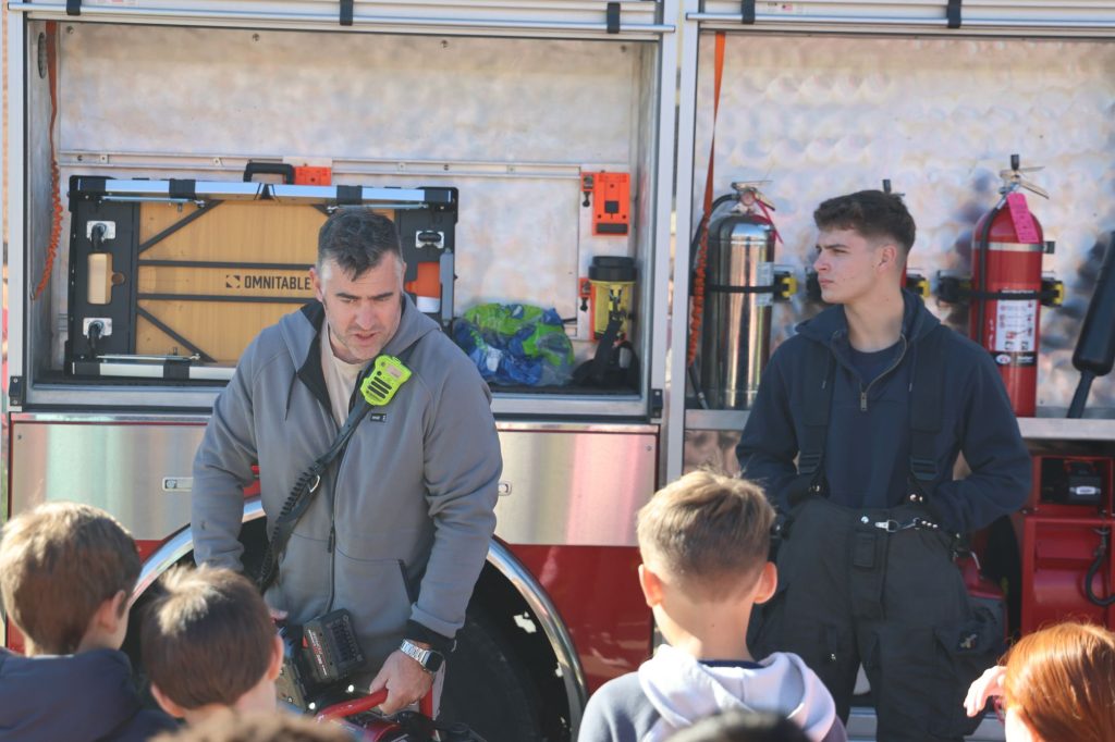 volunteer firefighters presenting fire truck equipment to elementary students