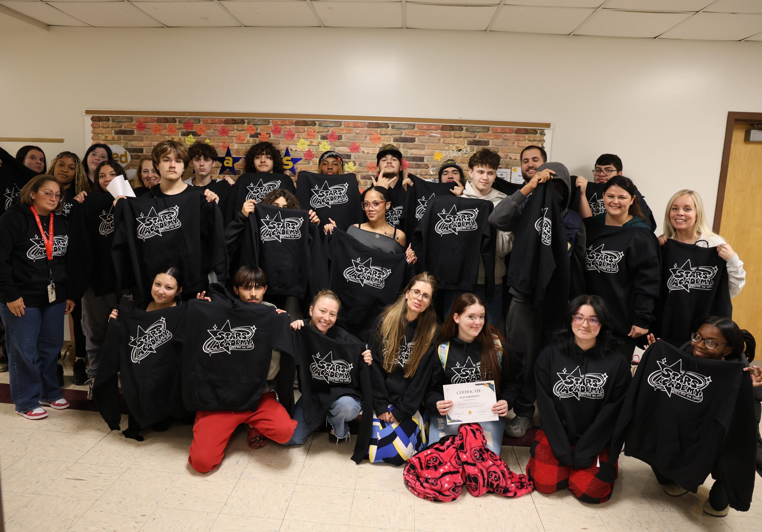 group photo of students and teachers holding sweatshirts