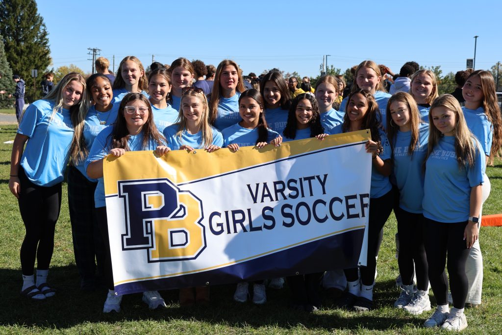 high schoolers standing for picture holding a varsity girls soccer banner