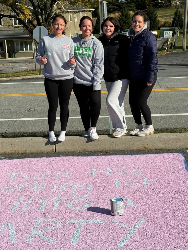 4 students standing in front of their painted parking spot